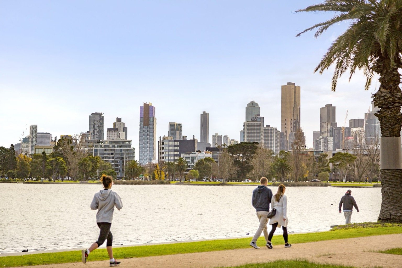 People enjoying a sunny day at Albert Park Lake, Melbourne, with city skyline in the background.