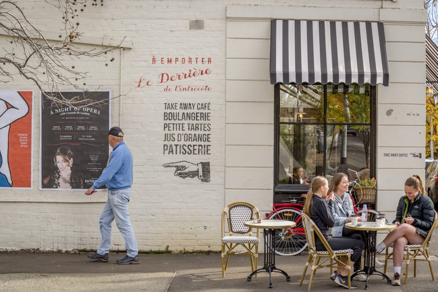 Outdoor cafe with people at tables, posters on the wall, and "TAKE AWAY CAFÉ" sign.