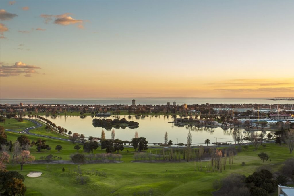 Albert Park Lake, Melbourne, Australia, with city skyline and Port Phillip Bay in the distance at sunrise.