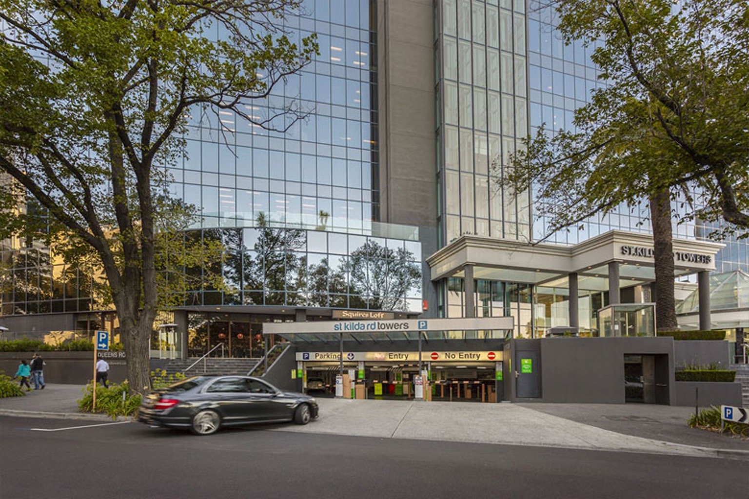 St Kilda Towers building entrance with Squires Loft sign, parking entry, and surrounding trees.