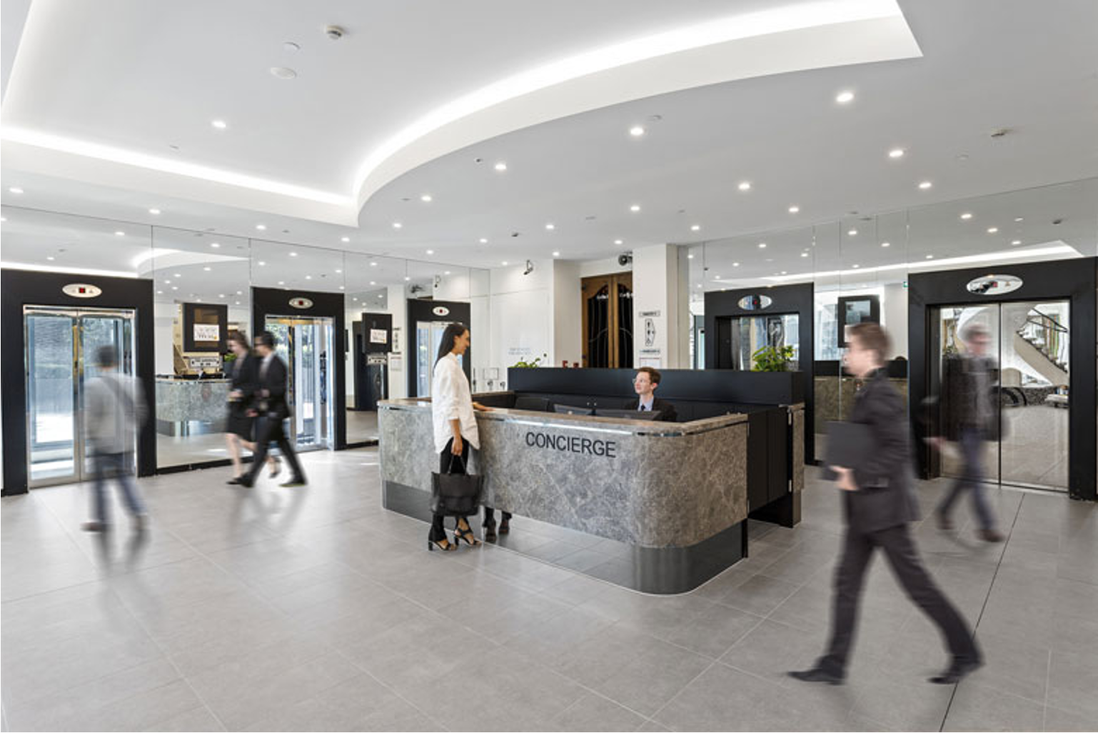 Modern office lobby with concierge desk and people walking by.
